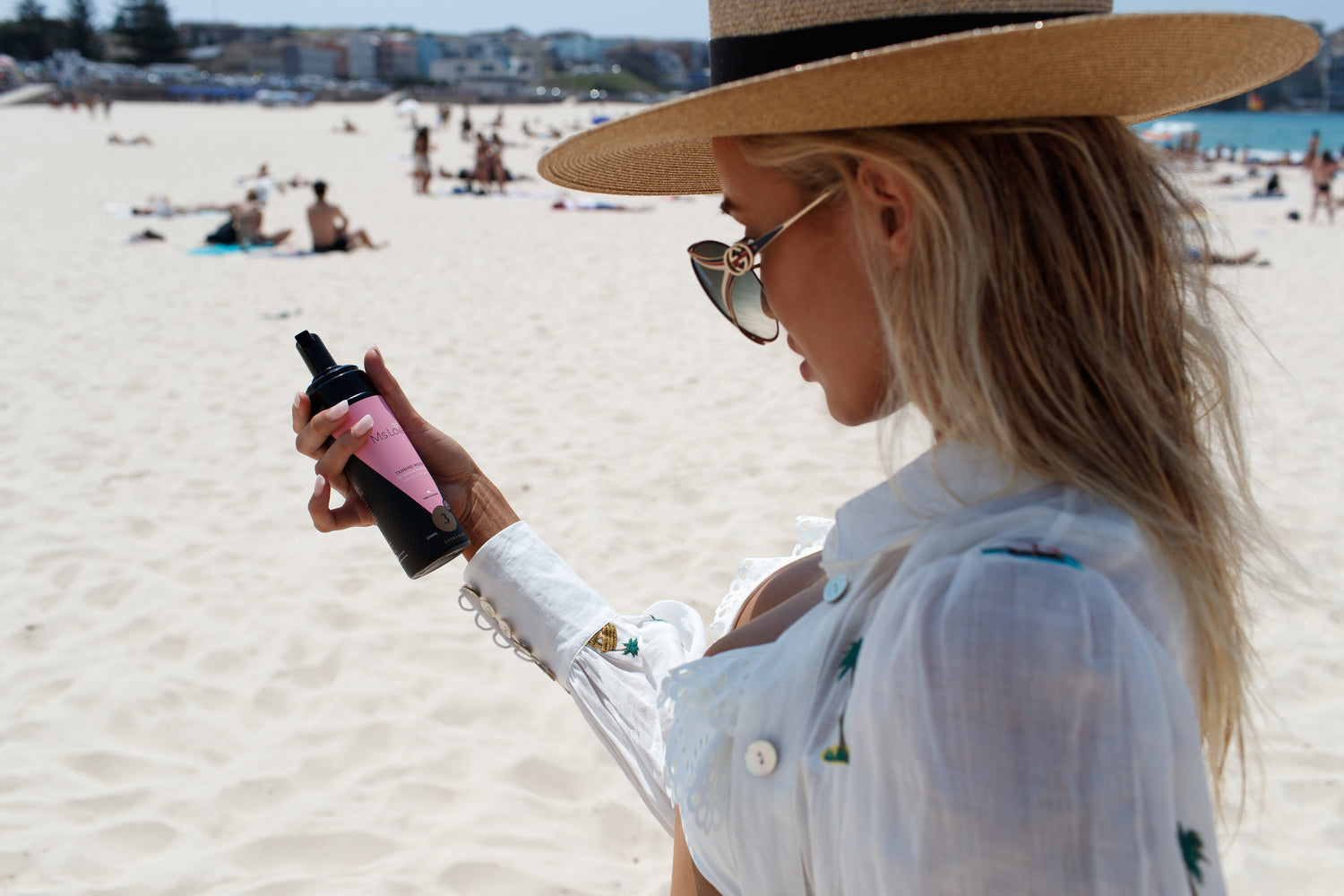 Woman at the beach holding Ms. Lova Extra Dark Tan Mousse, showing an even, sun-kissed glow.